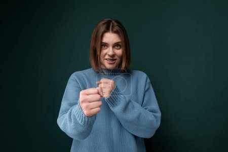 A woman wearing a blue sweater is seen in the picture, making a fist gesture. She appears to be demonstrating determination or strength with the gesture.
