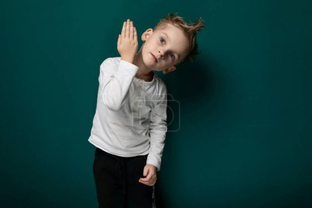 A young boy is seen standing confidently in front of a vibrant green wall, his hands resting casually in his pockets. The boy appears curious and observant, with a hint of determination in his
