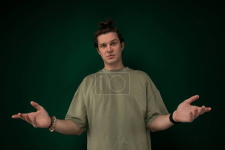 Photo for A man is standing in front of a green wall, extending both of his hands outwards. He appears to be in a posture of offering or greeting. - Royalty Free Image