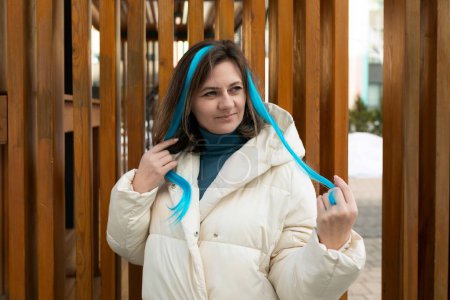 A woman wearing a white jacket stands out with her vibrant blue hair. She exudes confidence with her unique style and bold choice of hair color.