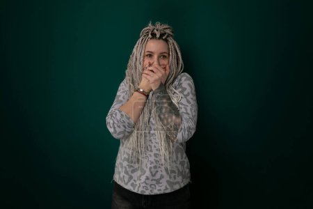 Una mujer con rastas sosteniendo sus manos sobre su cara en un gesto que expresa emoción o angustia. El foco está en sus manos y cabello, con su cara oscurecida.