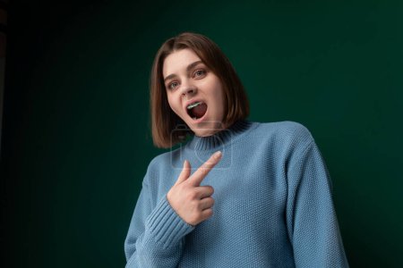 A woman wearing a blue sweater is pulling a comical expression, contorting her face in a humorous manner. She is playfully making a funny face, showcasing her sense of humor and lighthearted