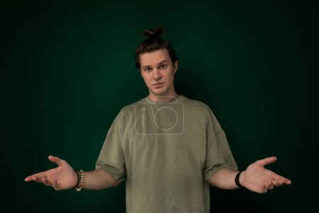 A man is standing in front of a green wall, extending both of his hands outward. He appears to be holding something or gesturing towards someone or something off-camera.