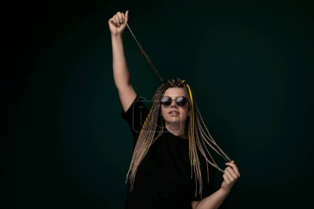 A woman with dreadlocks and stylish sunglasses is holding a string in her hand. She is looking directly at the camera with a confident expression, showcasing her unique style and personality.