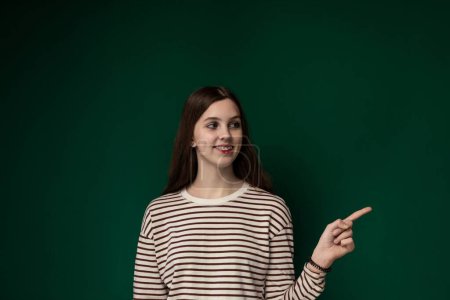 Photo for A woman is seen standing upright in front of a solid, green-painted wall. She appears calm and poised, her posture straight and composed. The wall provides a simple backdrop for the scene. - Royalty Free Image