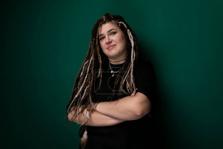 Photo for A woman with dreadlocks is shown standing in front of a bright green wall. She appears confident and is looking directly at the camera, with her hair hanging down in long, thick sections. The green - Royalty Free Image