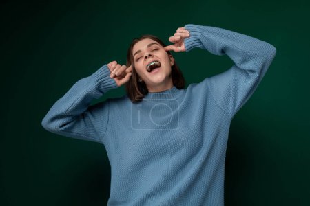 Auf dem Bild ist eine Frau im blauen Pullover zu sehen, die mit der Hand eine Geste macht. Ihr Gesichtsausdruck wirkt fokussiert, während sie durch die Geste kommuniziert, die sie macht.