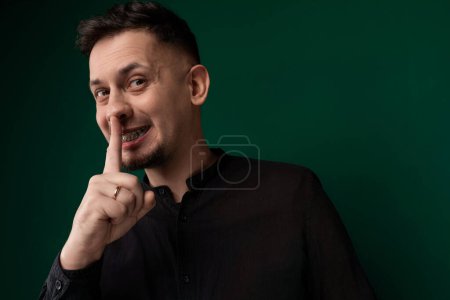 Un hombre está haciendo humorísticamente una cara mientras sostiene su dedo a sus labios en un gesto lúdico, posiblemente indicando silencio o secreto. Su expresión es cómica y exagerada, añadiendo un sentido de