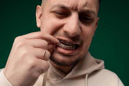 Un hombre con una sudadera con capucha blanca está parado frente a un fregadero y cepillándose los dientes con pasta de dientes en un cepillo de dientes. Se centra en su reflejo en el espejo mientras realiza su oral matutino