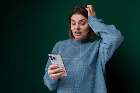 Una mujer con un suéter azul sostiene un teléfono celular en sus manos. Parece estar involucrada con el dispositivo, posiblemente enviando mensajes de texto o navegando. El fondo está borroso, centrándose en la mujer y su