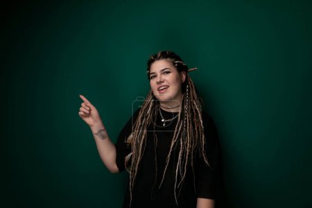 Photo for A woman with dreadlocks is pointing at something off-camera. She appears to be engaging in a conversation or directing attention towards a specific object. Her facial expression indicates focus and - Royalty Free Image