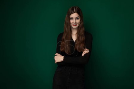 Photo for A woman stands confidently with her arms crossed in front of a vibrant green background, exuding a sense of determination and strength. Her posture conveys self-assurance and independence. - Royalty Free Image