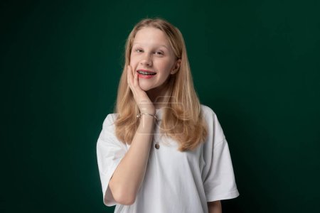 Une jeune fille, peut-être une adolescente, pose pour une photo devant un fond vert vibrant. Elle semble confiante et sourit pour la caméra.