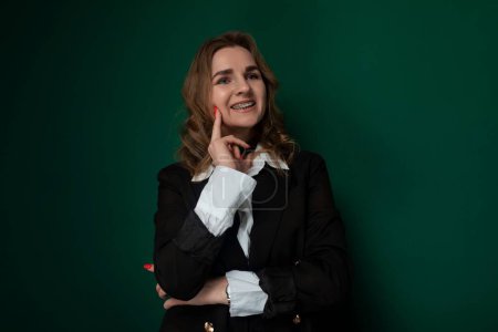 Une femme se tient debout devant un mur vert, prenant une pose pour une photo. Elle semble confiante et élégante, avec un sourire éclatant sur son visage.