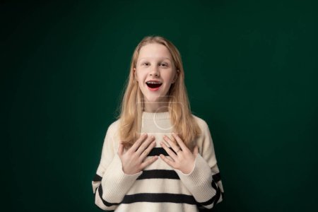 Ein junges Mädchen steht vor leuchtend grünem Hintergrund und verzerrt ihr Gesicht zu einem komischen Ausdruck. Sie wirkt verspielt und animiert, als sie ihre albernen Eskapaden zur Schau stellt.