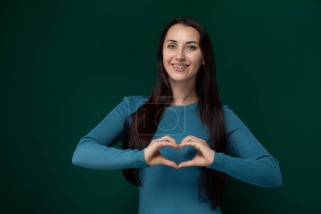Una mujer está de pie y formando una forma de corazón con sus manos en esta imagen. Ella está usando ambas manos para crear el símbolo de un corazón.