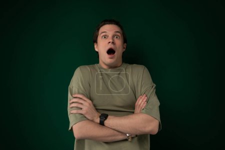 A man is standing in front of a green wall, looking surprised. His facial expression conveys shock or disbelief.