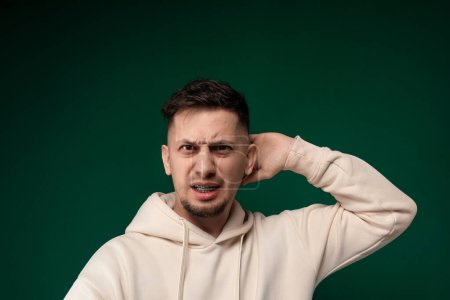 Un homme portant un sweat à capuche blanc se tient les mains contre les oreilles. Il semble se couvrir les oreilles, peut-être en réponse à un bruit fort ou à une gêne.
