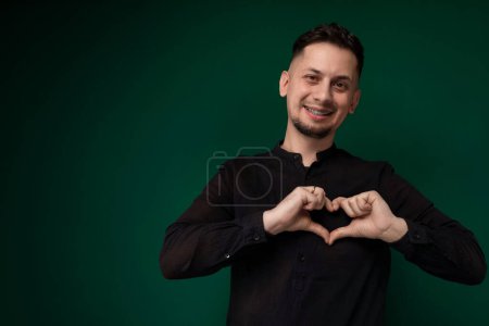 A man standing and forming a heart shape with his hands. His fingers are interlocked to create the symbol of love or affection. The background is simple, allowing the focus to remain on the hand