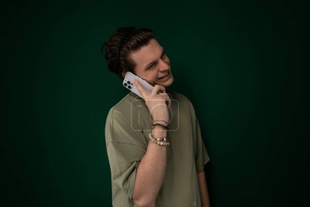 A man wearing a dark jacket is standing outdoors while speaking on a cell phone. He appears focused and engaged in the conversation, with his hand holding the phone to his ear. The background shows a