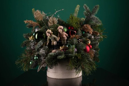 Un arrangement de vacances festive mettant en vedette des ours en peluche câlins et des ornements étincelants en rouge, vert et or. Les ours en peluche portent des chapeaux de Père Noël et les ornements sont délicatement placés autour