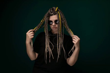 A man with dreadlocks is holding his long hair in front of his face, covering his features. His hair is styled in thick, twisted strands that reach down to his chest. The mans face is partially