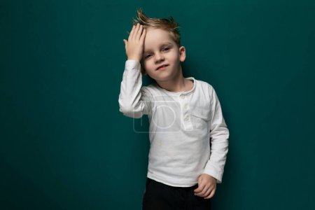A young boy stands in front of a vibrant green wall, looking curious and adventurous. The boys small stature contrasts with the tall structure behind him, creating a sense of scale and perspective.