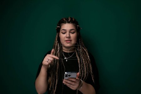 A woman with dreadlocks is seen looking intently at her cell phone screen, engrossed in whatever is displayed. Her hair is styled in intricate dreadlocks, and her focus is solely on the device in her