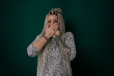 Photo for A woman is shown covering her mouth with both hands. Her facial expression suggests shock, surprise, or horror. The action conveys a sense of secrecy or suppression. - Royalty Free Image