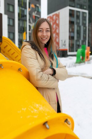 A woman is standing in front of a bright yellow object. She appears contemplative, looking towards the object. The scene is simple yet striking, with the contrast between the woman and the vibrant