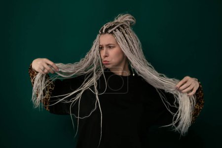 Photo for A woman with long hair is holding onto her strands, showcasing their length and texture. Her hair cascades down her back, emphasizing its thickness and healthy appearance. - Royalty Free Image