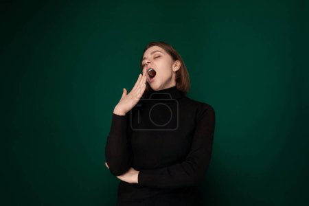 Une femme portant une chemise noire est montrée la bouche ouverte. Elle tient sa bouche large avec sa main dans un geste de surprise ou de choc.