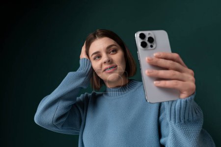 Eine Frau hält ein Handy vor ihr Gesicht, lächelt und posiert für ein Selfie. Sie benutzt die Frontkamera, um sich im Moment selbst festzuhalten.