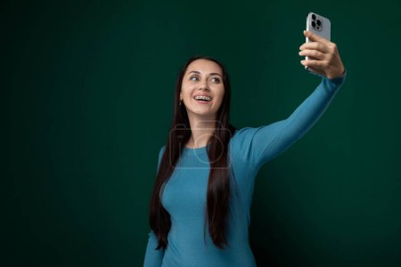 Una mujer sostiene un teléfono celular y se toma una foto. Ella se ve sonriendo en la pantalla del teléfono mientras captura la selfie.