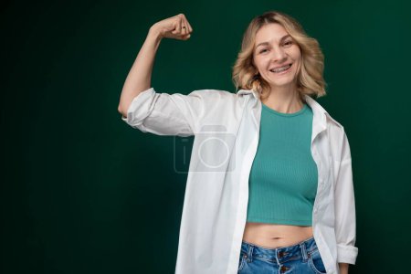 Una mujer de pie con confianza con el puño levantado en una pose para una foto. Se ve fuerte y decidida, mostrando empoderamiento y resiliencia.