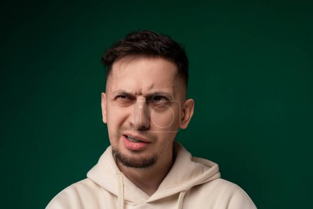 Photo for A man wearing a hoodie is contorting his face, showcasing various expressions such as grimacing, wincing, and squinting. His facial features are highlighted by the hoodies shadow. - Royalty Free Image