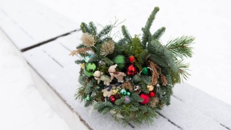 A Christmas wreath is placed on top of a weathered wooden bench, adding a festive touch to the rustic setting. The wreaths vibrant colors contrast with the benchs natural wood tones.