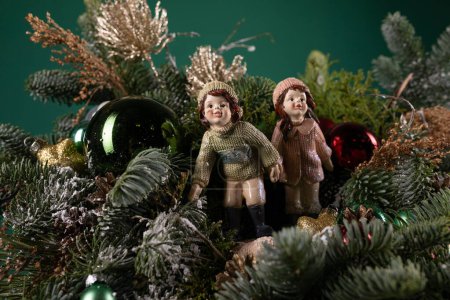 Two figurines, one male and one female, are positioned on the highest point of a beautifully decorated Christmas tree. The couple is wearing festive attire and appear to be holding hands, adding a