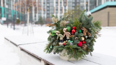 A potted plant adorned with Christmas decorations sits on a ledge. The decorations include ornaments, lights, and ribbons, adding festive cheer to the setting. The plant looks healthy and vibrant