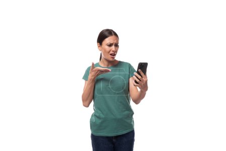 attraktive junge kaukasische Frau mit schwarzen Haaren im T-Shirt schaut aufmerksam zum Telefon.