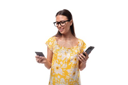 young brunette woman with straight hair dressed in a casual yellow T-shirt looks at the bank card data in her hands to use banking on her phone.