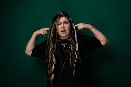A woman with long dreadlocks is shown in the photograph, contorting her facial expression. Her facial features are exaggerated as she grimaces or makes a funny face, showcasing the flexibility of her