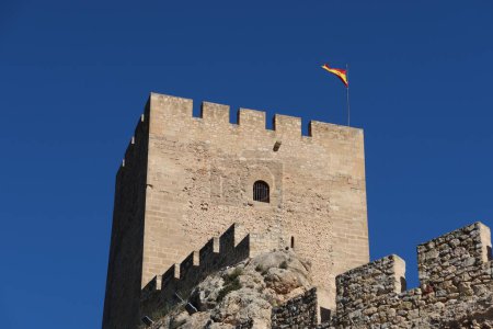 Sax, Alicante, Spain, March 12, 2024: Flag of Spain on the tower of the Almohad castle of Sax on top of a rock. Sax, Alicante, Spain