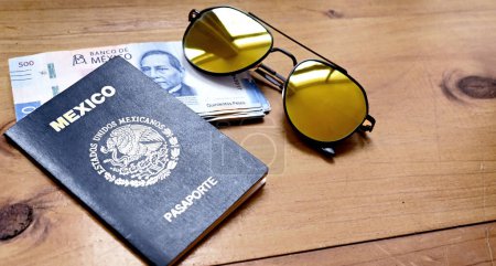 Téléchargez les photos : Scene of a Mexican passport with a bundle of Mexican bills and sunglasses on a wooden table, concept of vacations. - en image libre de droit