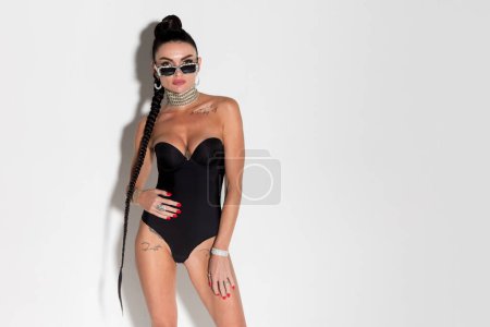 Foto de Morena sensual mostrando su cuerpo delgado y cerraduras que fluyen en lencería negra, exudando encanto en un rodaje de estudio bañado en tonos cálidos. - Imagen libre de derechos