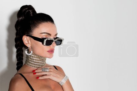 Photo for With poise and style, a woman wearing sunglasses and sporting a long ponytail poses for a close-up portrait in the studio, her glamorous appearance capturing attention - Royalty Free Image