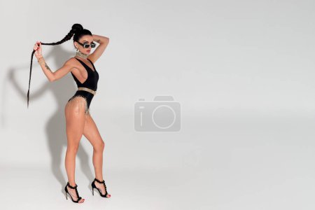 Photo for With elegance and allure, a slender woman slowly removes her attire to unveil sleek black lingerie, her taut body and long ponytail capturing attention in the warm ambiance of the studio - Royalty Free Image