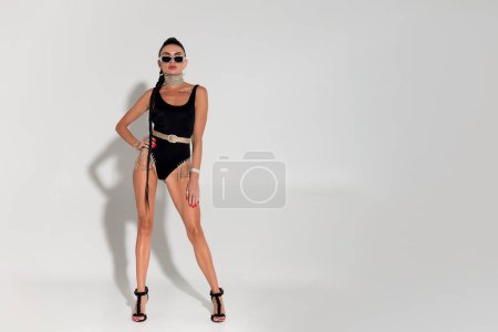 Photo for Posing with allure and grace, a slender lady undresses to reveal her chic black lingerie in the warm glow of the studio, her taut body and long ponytail capturing attention with every movement - Royalty Free Image