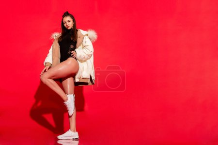 Photo for Confident and stylish, a young girl poses in the studio against a striking red backdrop, her chic white jacket making a bold fashion statement - Royalty Free Image