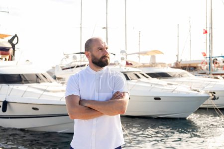 Téléchargez les photos : Élégance captivante : un homme suave pose à côté de son yacht de luxe au port, mettant en valeur la quintessence du luxe maritime - en image libre de droit